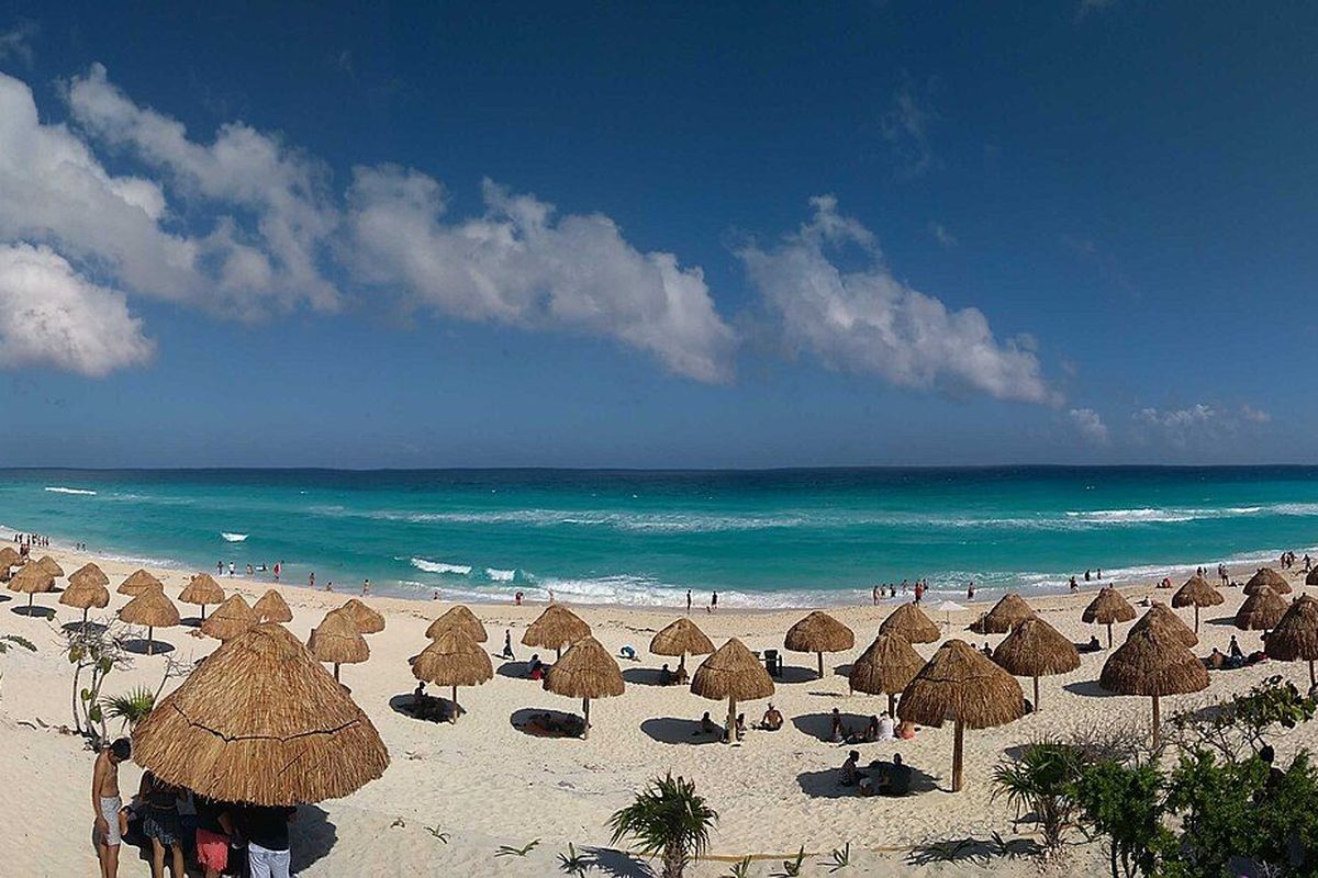 Thatched parasols on white sand above turquoise Caribbean water at Cancún