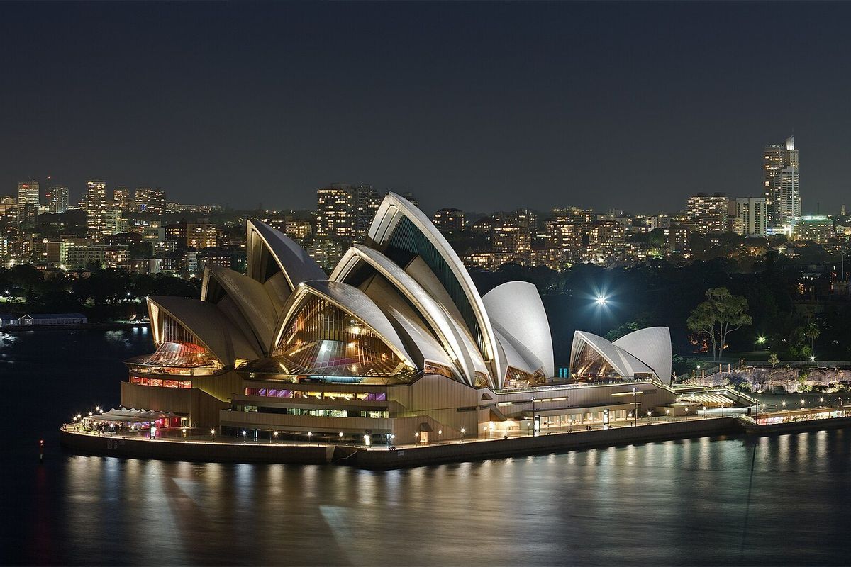 Sydney Opera House lit at night on the harbour, with the city behind